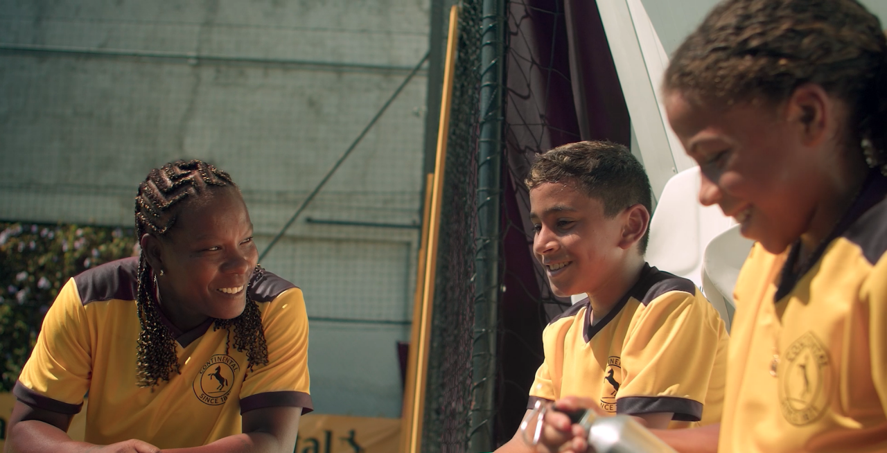 (Imagem da lenda do futebol feminino, "Formiga", um menino e uma menina conversando sorrindo. Todos com uniforme de futebol da Continental Pneus)
