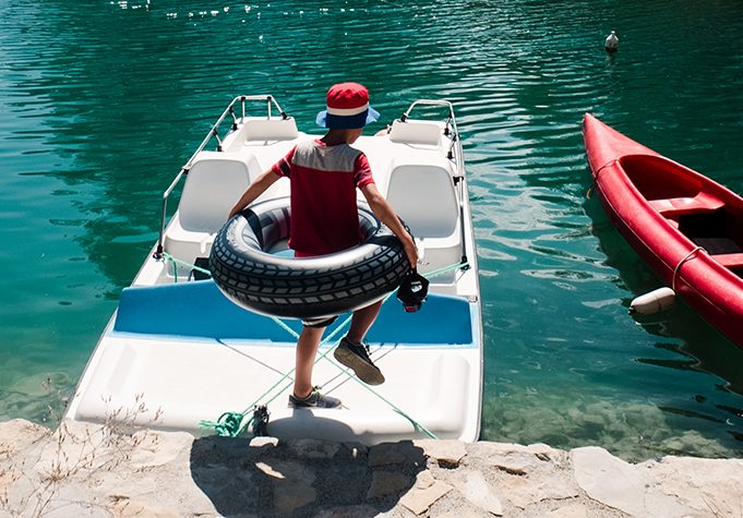 (Criança correndo com boia em direção a barco em lago)