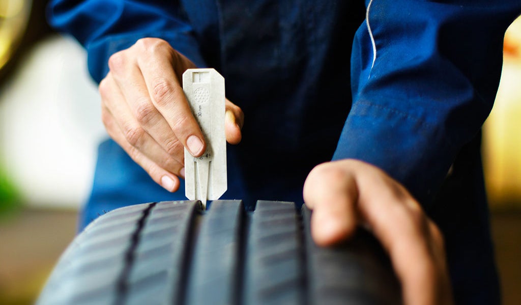 (foto de pessoa com macacão azul utilizando o profundímetro no sulco de um pneu de carro)