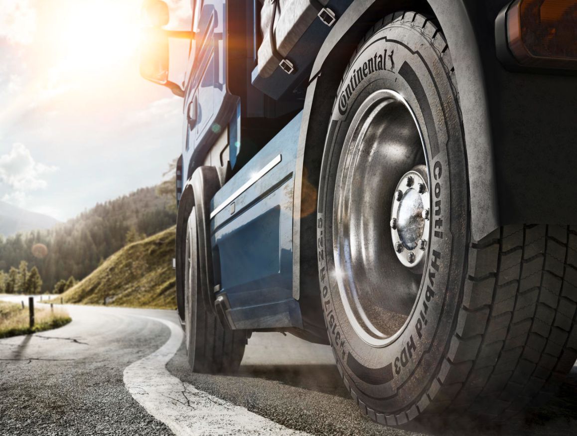 (foto de caminhão em close no pneu trativo da Continental instalado no cavalo - fundo de dia ensolarado, montanhas e estrada curva)