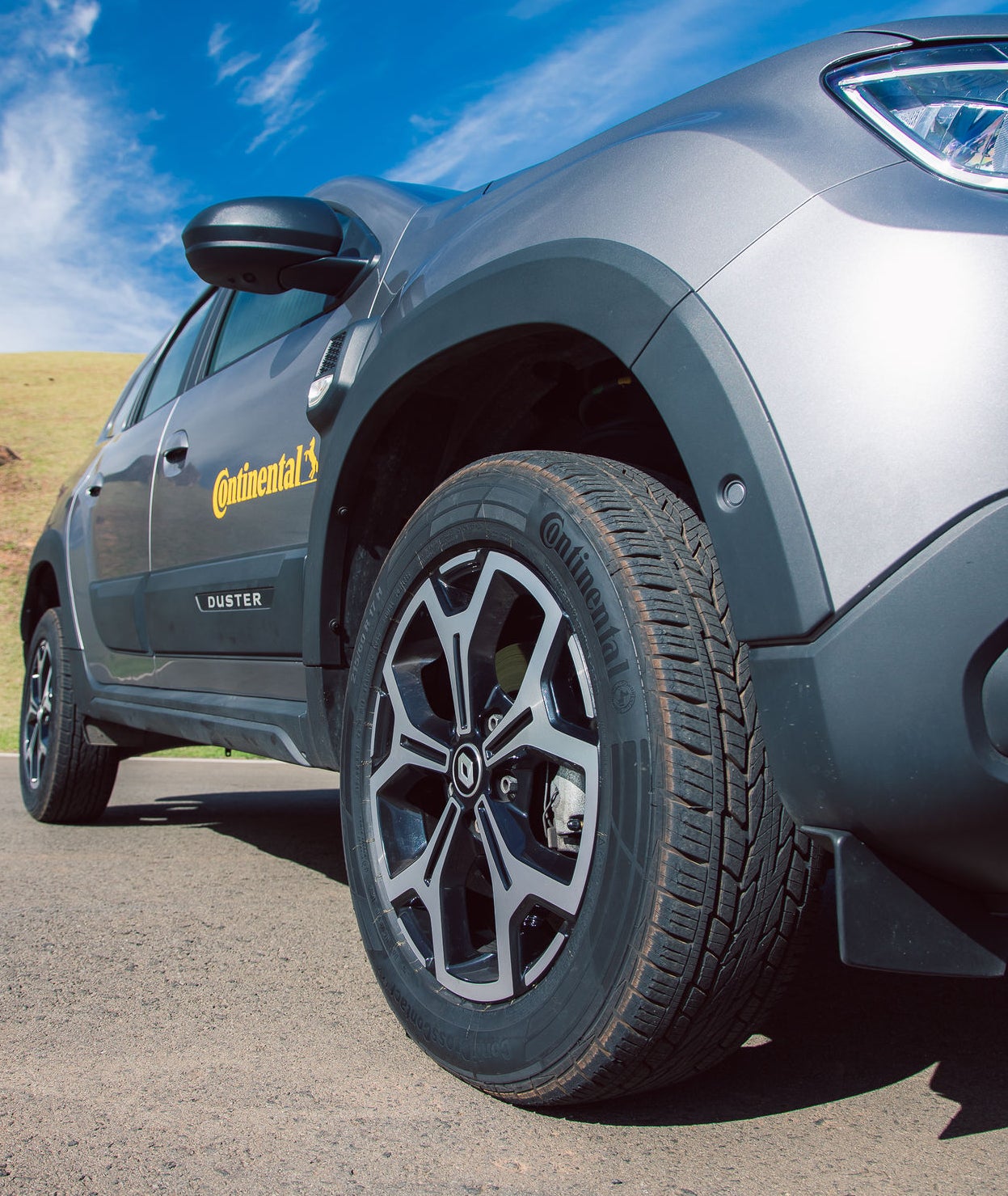 (foto da Duster cinza com adesivo da Continental na porta, com close no pneu dianteiro)