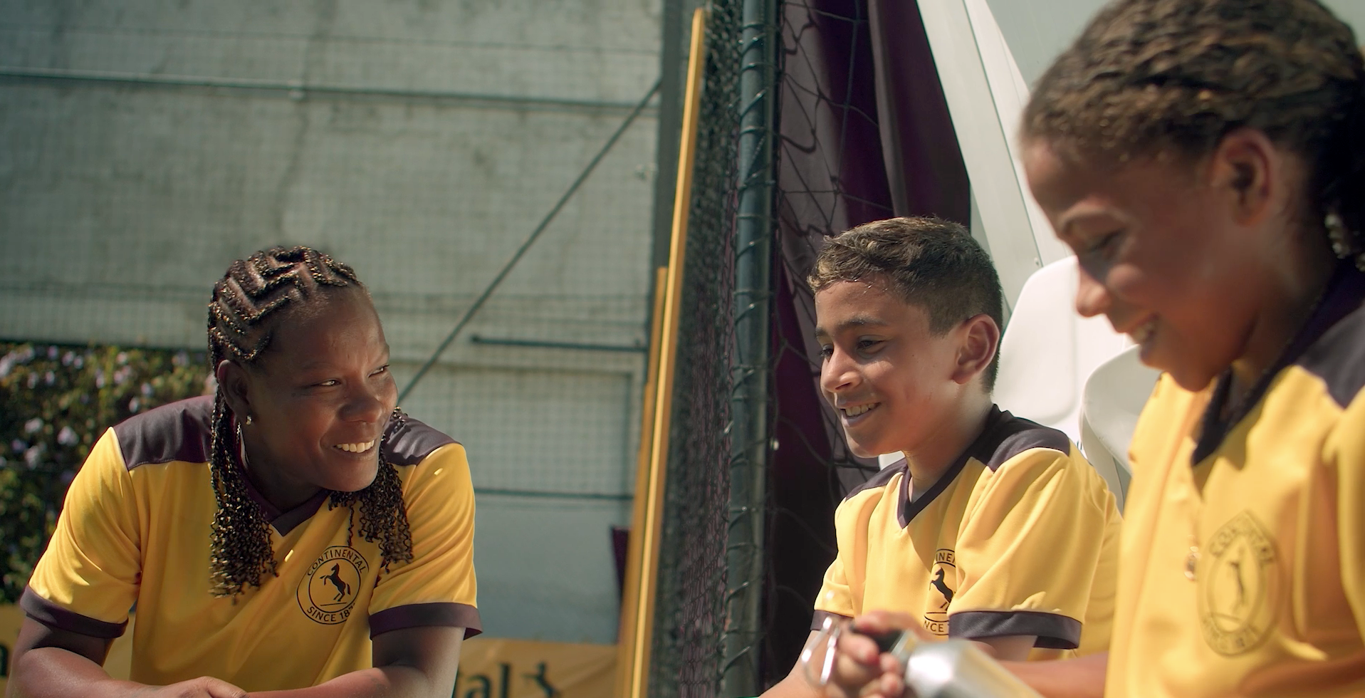 (Imagem da lenda do futebol feminino, "Formiga", um menino e uma menina conversando sorrindo. Todos com uniforme de futebol da Continental Pneus)