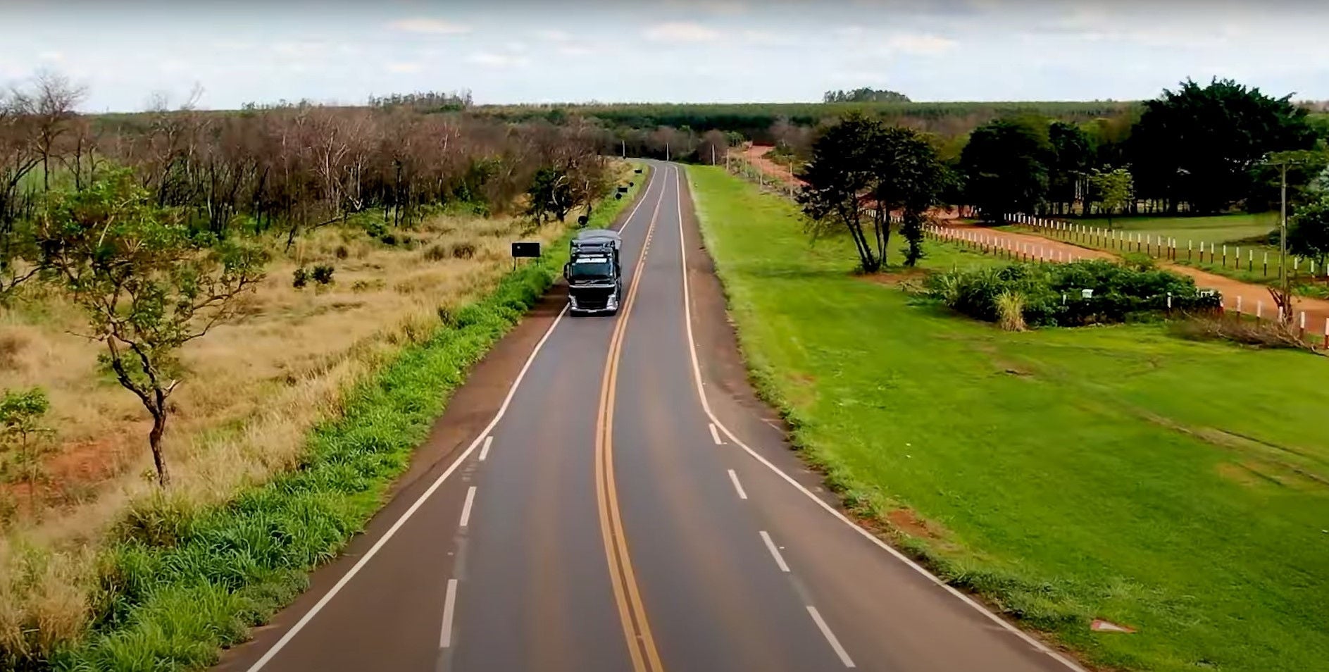 (foto estrada com fazendas ao lado e caminhão andando na estrada)