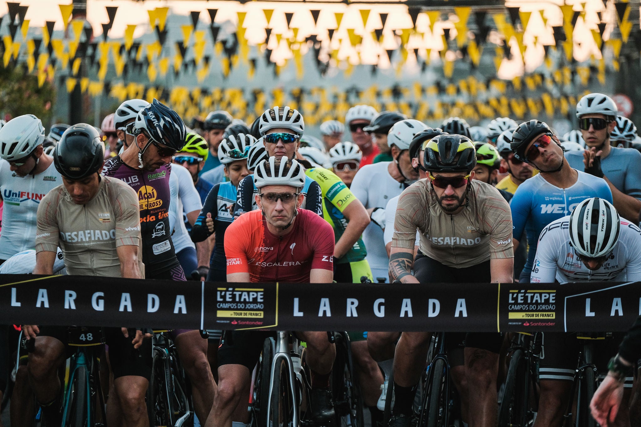 (foto de diversos ciclistas parados atrás da facha de largada do evento)