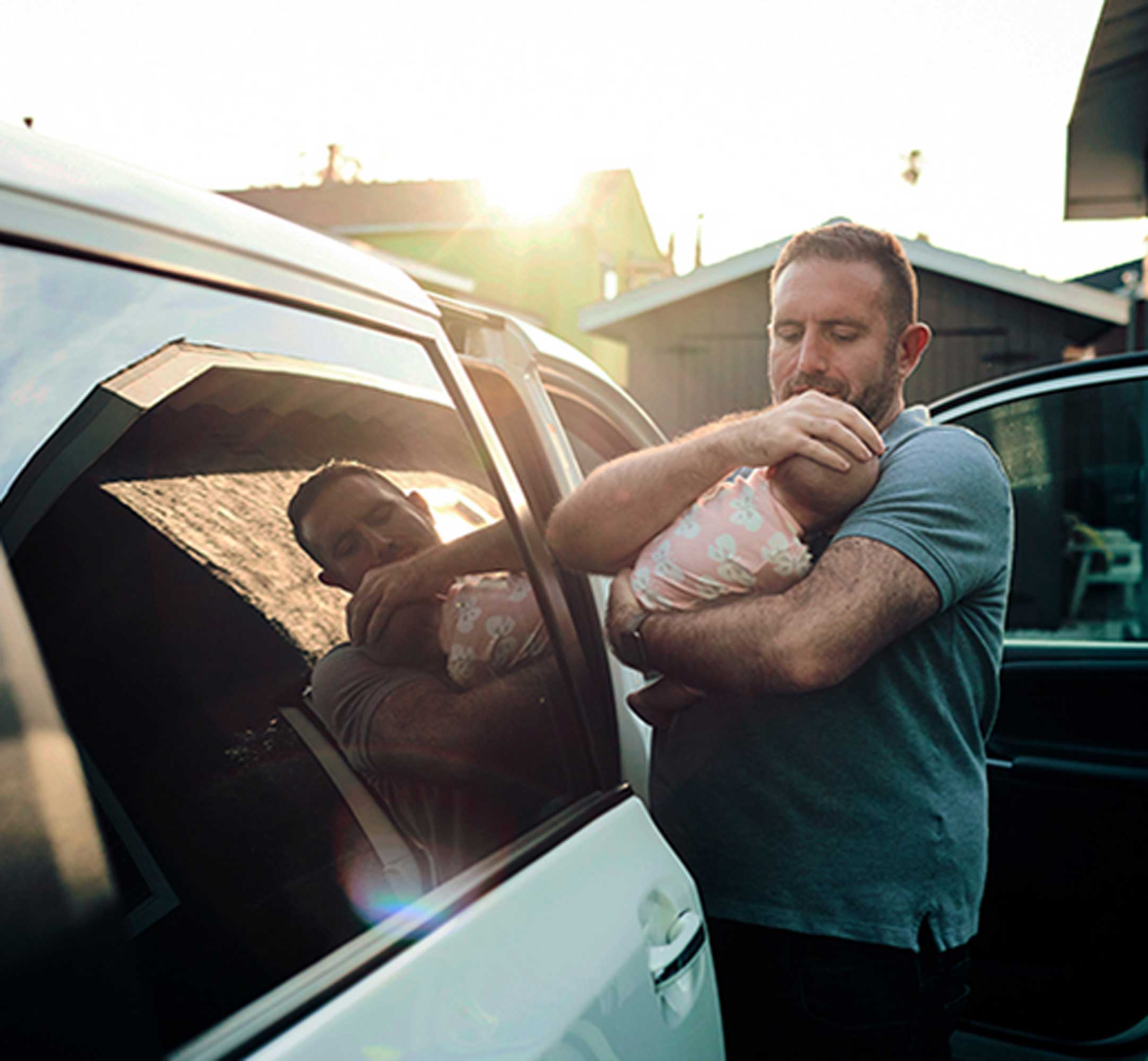 (Pai protegendo a cabeça do bebê no colo enquanto entra no carro)