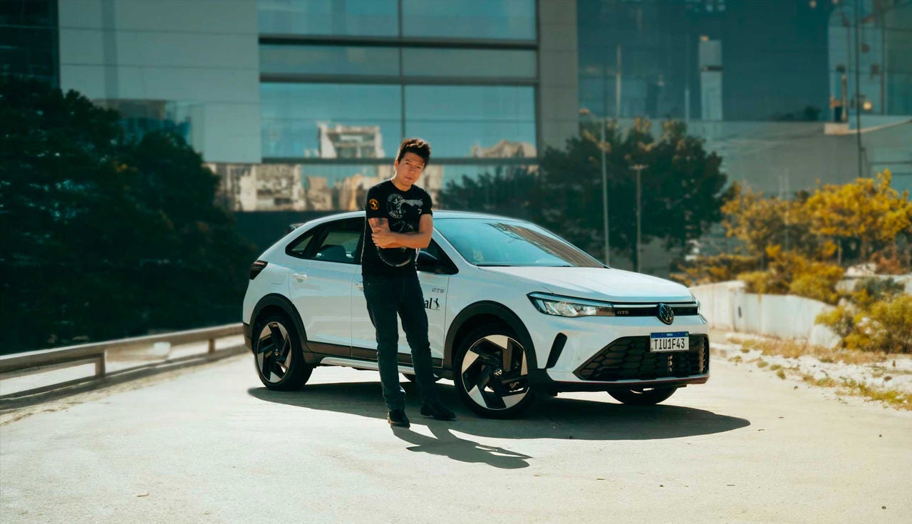 (Juliano Barata, Homem em pé ao lado de um Volkswagen Nivus GTS 2025 branco, equipado com rodas esportivas e pneus Continental, em um ambiente urbano com prédios ao fundo. A imagem destaca o visual moderno e esportivo do veículo)