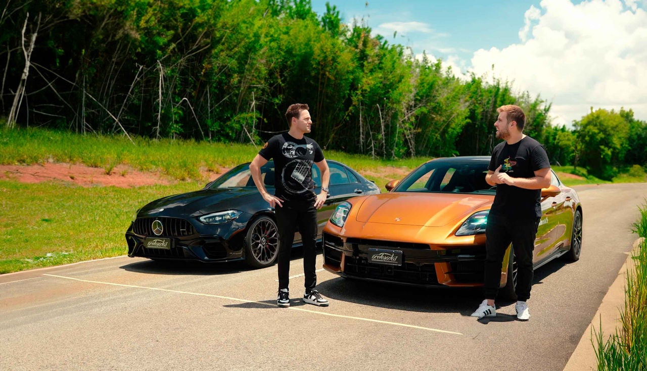 (A imagem mostra dois homens brancos de pé em uma estrada, cercados por um ambiente natural. À esquerda, há um Mercedes-AMG C 63  preto, de design elegante e um visual robusto. À direita, um Porsche Panamera 4S Hybrid laranja brilhante, com um perfil aerodinâmico. Ambos os veículos estão estacionados em uma área aberta, com grama verde ao fundo e algumas árvores ao longe. Os homens estão conversando e parecem se divertir. Um deles usa uma camiseta preta com um desenho de pneu esportivo da Continental, enquanto o outro veste uma camiseta preta com detalhes coloridos. O dia está ensolarado e o céu apresenta algumas nuvens brancas)