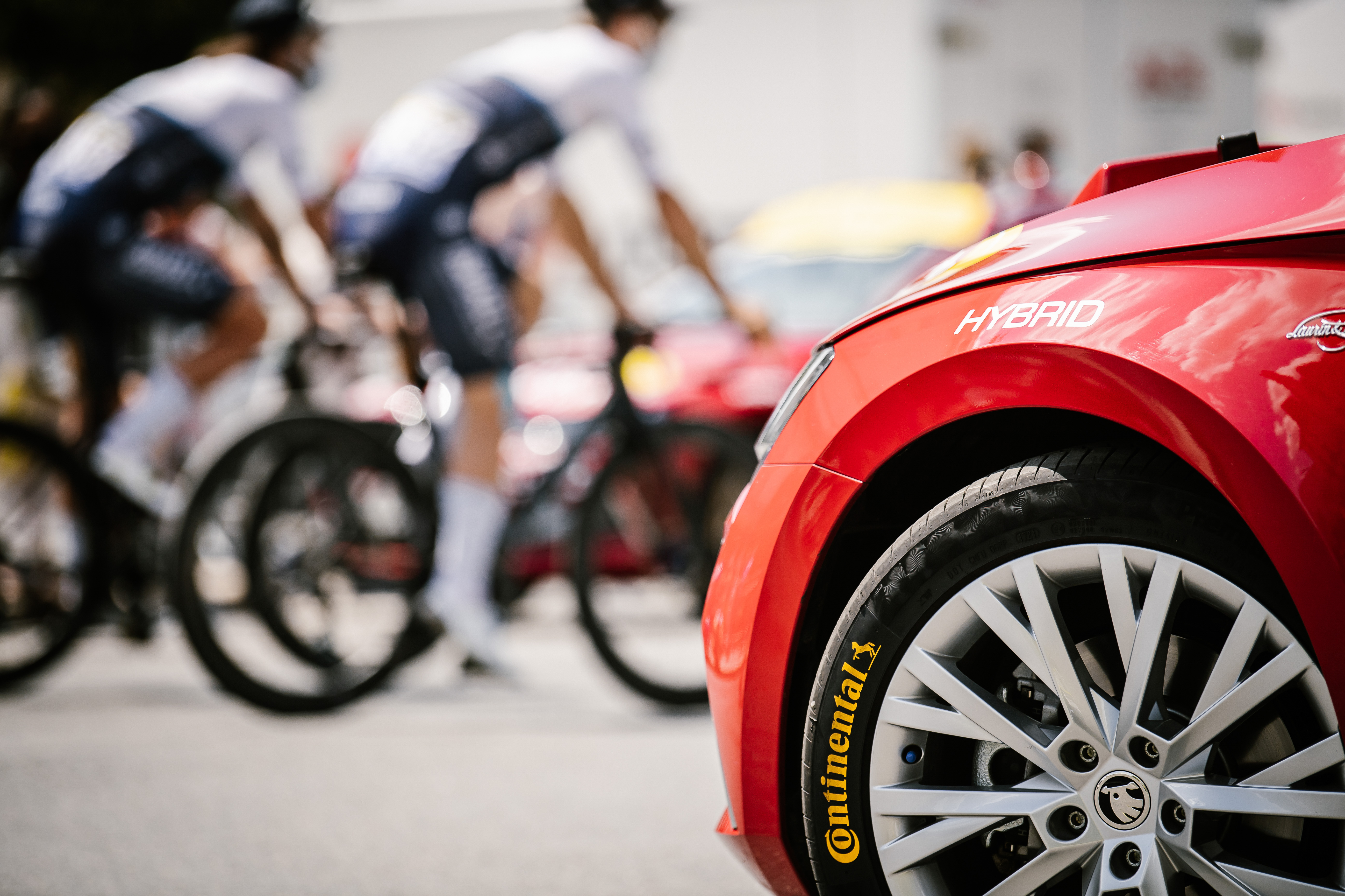 (imagem de ciclistas durante evento do Tour de France e carro vermelho oficial da competição com pneus da Continental)