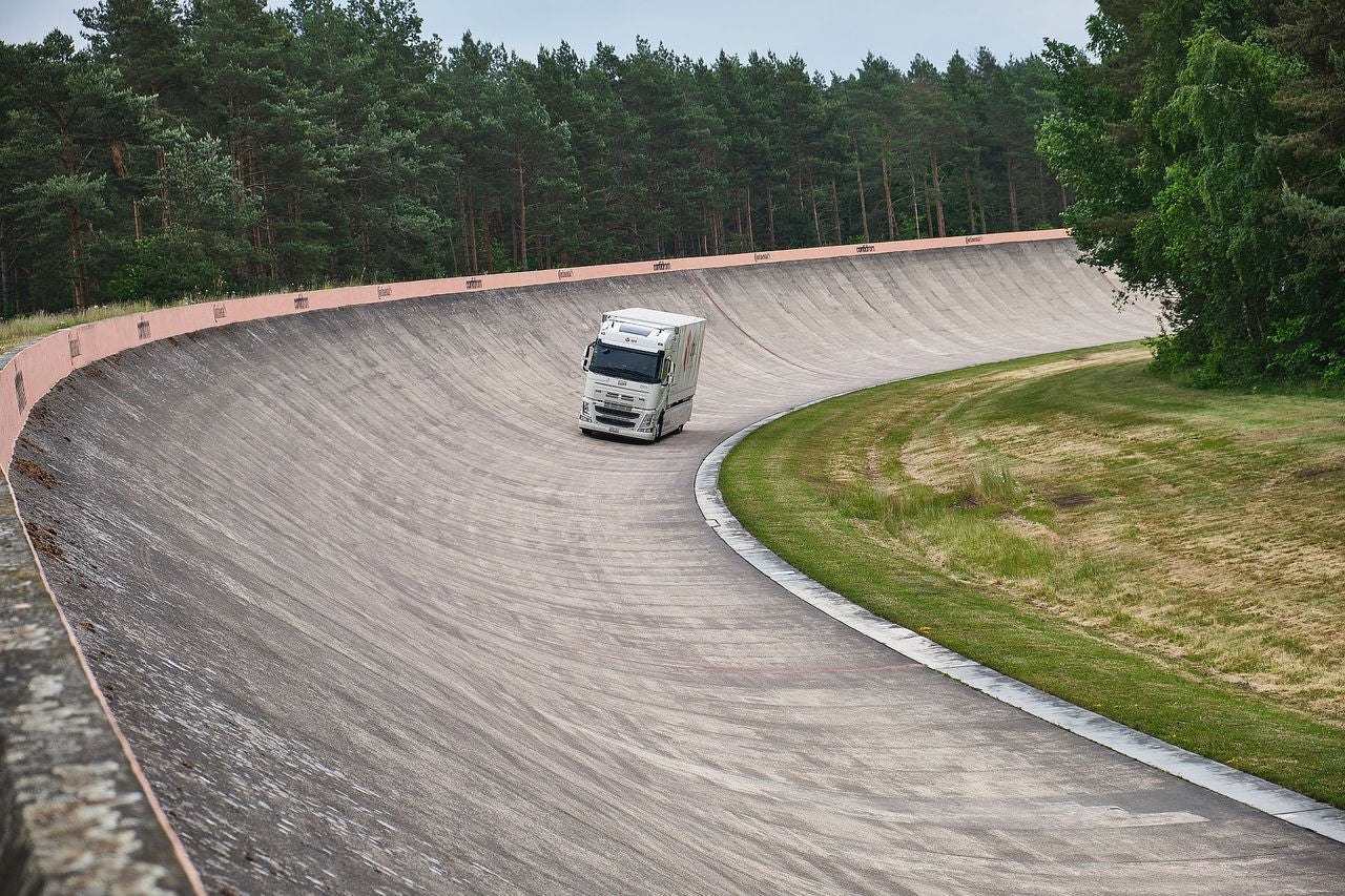 (imagem distante de um caminhão baú branco, com pneus Continental e adesivo da dpd na lateral andando na parte curvada da pista de teste Contidom da Continental)