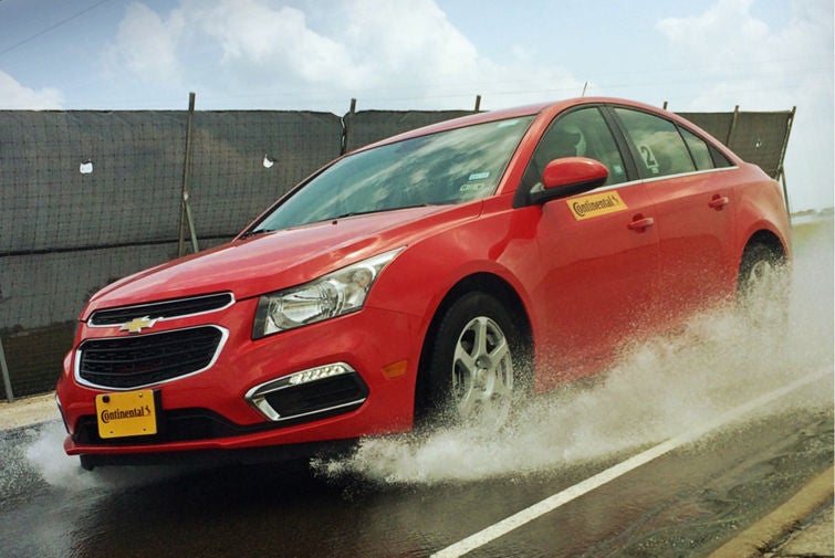 (foto de carro sedan vermelho com placa da Continental, andando em pista molhada durante chuva)