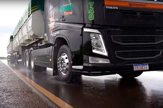 (foto de caminhão preto andando em asfalto durante chuva leve)