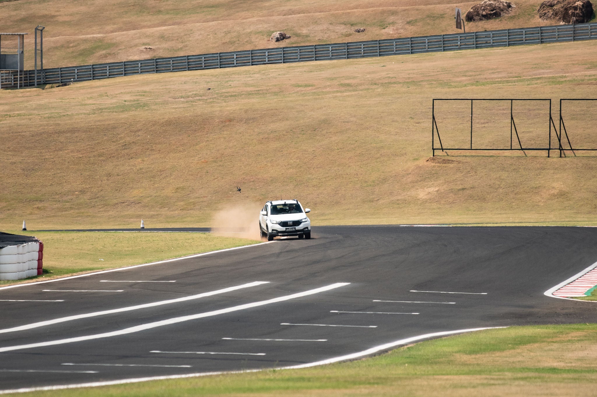 (foto aérea de Nova Strada branca calçada com pneus da Continental, andando em pista e passando em trecho de terra, levantando poeira ao passar)