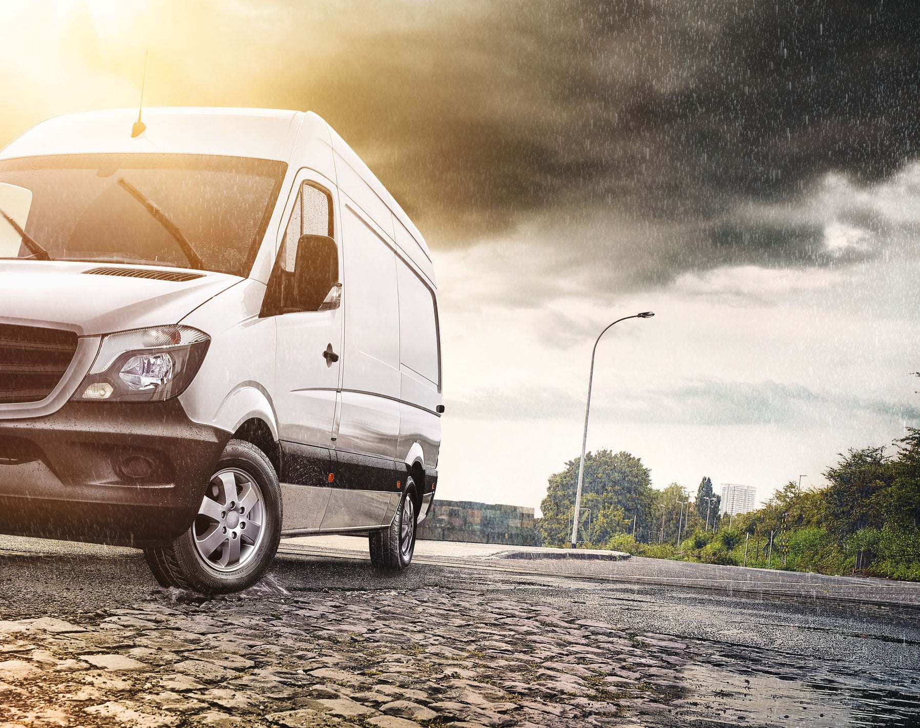 (foto de van com pneus Continental parada em terreno de paralelepípedo durante chuva e por do sol) 