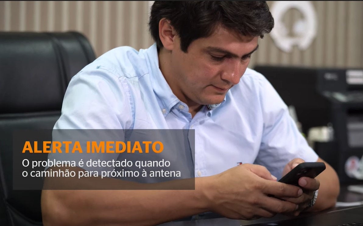 (foto de homem branco, cabelo castanho escuro, sem barba, com camisa azul clara, sentado em poltrona enquanto usa celular)