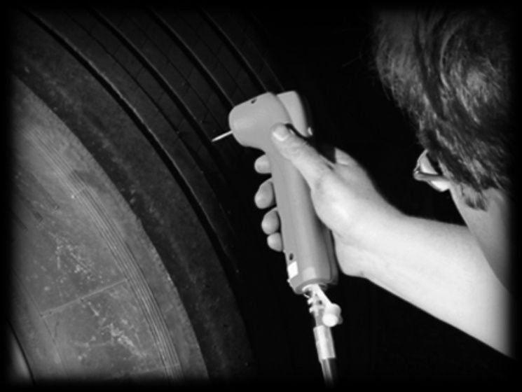 (foto em preto e branco de homem com ferramenta ContiTrack 2 em mãos enquanto inspeciona o sulco de um pneu de carga)