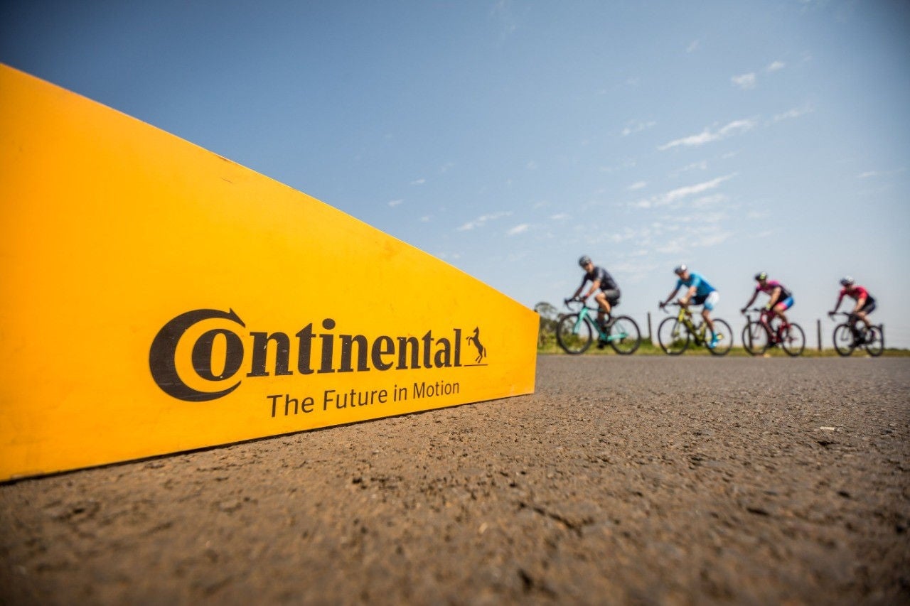 (imagem de placa laranja com logotipo Cnotinental + ciclistas ao fundo durante evento do Brasil Ride)