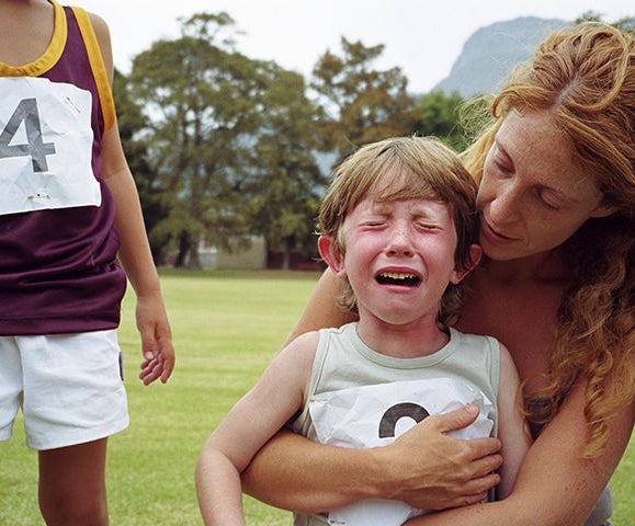 (criança chorando nos braços da mãe em campo gramado durante campeonato)