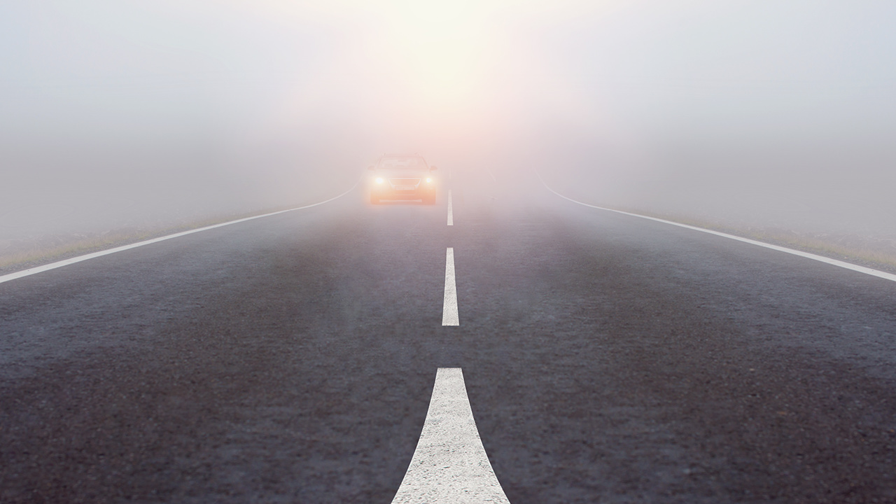 Car drives on road through fog