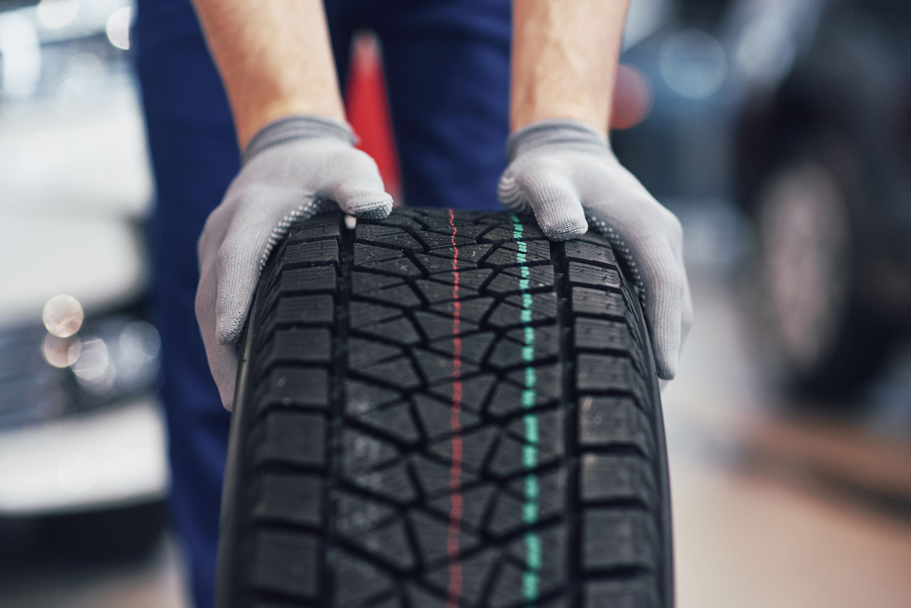 Closeup of mechanic hands pushing a black tire in the workshop.