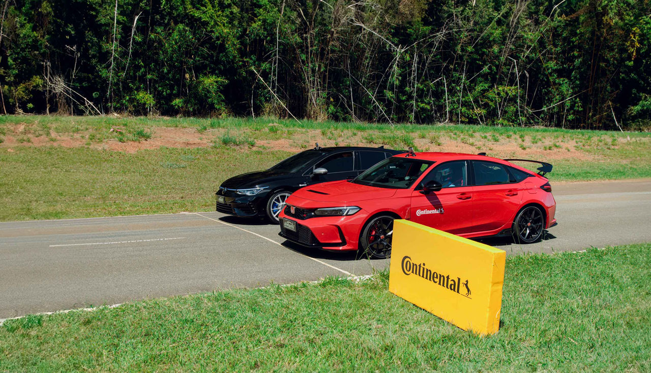 (Honda Civic Type R vermelho e Volkswagen Golf R preto alinhados em pista de arrancada para teste de performance, ambos equipados com pneus Continental SportContact 7. A imagem mostra o cenário em ambiente ensolarado, com destaque para a marca Continental Pneus em uma placa amarela à frente dos carros, rodeados por vegetação ao fundo)