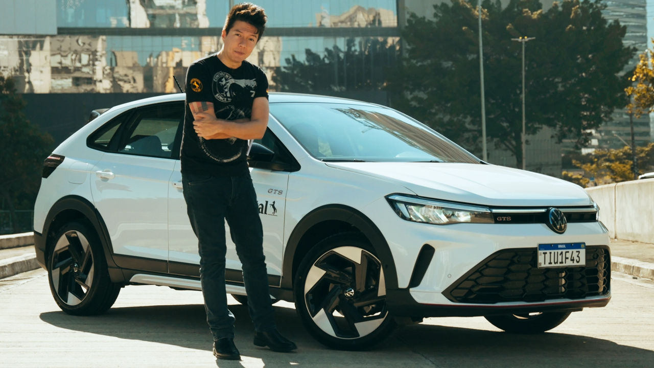 (Juliano Barata, Homem em pé ao lado de um Volkswagen Nivus GTS 2025 branco, equipado com rodas esportivas e pneus Continental, em um ambiente urbano com prédios ao fundo. A imagem destaca o visual moderno e esportivo do veículo)