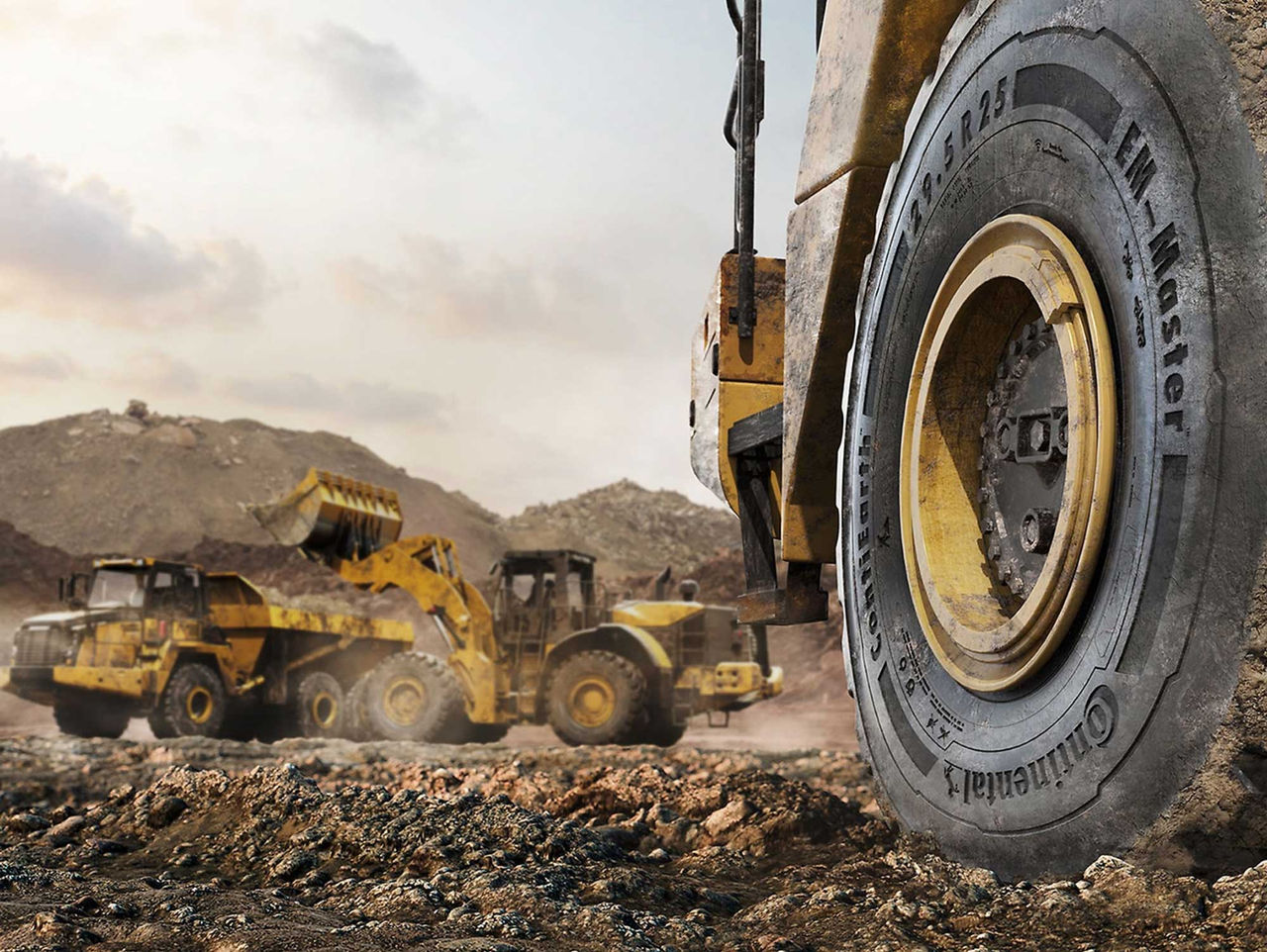 (A imagem retrata um cenário de mineradora. Em primeiro plano, vemos o pneu Continental OTR de uma máquina grande, com características robustas, sugerindo um ambiente de trabalho intenso e extremo. O pneu é negro com detalhes em amarelo, indicando a marca Continental. A parte de trás mostra três máquinas pesadas, como carregadeiras e caminhões, que estão trabalhando em um terreno irregular e acidentado. O solo é de terra, com algumas pedras visíveis e uma coloração marrom, indicando que o local está sendo escavado ou nivelado. O céu ao fundo é levemente nublado, com tons claros de azul e cinza, e a atmosfera sugere um dia de trabalho ativo, com poeira no ar, proveniente do movimento das máquinas. A cena transmite uma sensação de grandeza e atividade industrial)